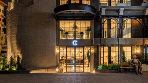 A hotel entrance with a stone facade, a glass door with a logo, and a bench with a statue. - Chateau Du Village Patong (Patong)