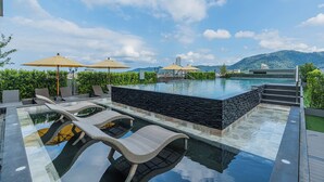 A modern infinity pool with lounge chairs and umbrellas, surrounded by greenery and a mountain view. - Chateau Du Village Patong (Patong)