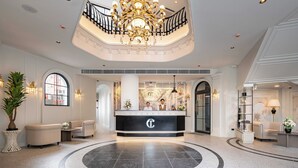 A hotel lobby with a reception desk, two receptionists, a chandelier, and a circular floor design. - Chateau Du Village Patong (Patong)
