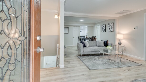 A modern living room with a grey sofa, a glass coffee table, and a rug. There is a dining area in the background with a table and chairs. - ATL Oasis: Home Away From Home (Atlanta)