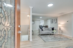 Un salon moderne avec un canapé gris, une table basse en verre et un tapis. On aperçoit à l’arrière-plan un coin repas avec une table et des chaises.
