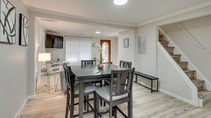 A dining area with a dark wooden table and chairs, a lamp, and a vase with flowers. There is a staircase to the right and a door leading to another room. - ATL Oasis: Home Away From Home (Atlanta)