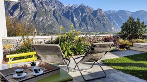 Une terrasse avec deux chaises et une table, un plateau avec des tasses et une cafetière, et une vue sur la montagne.