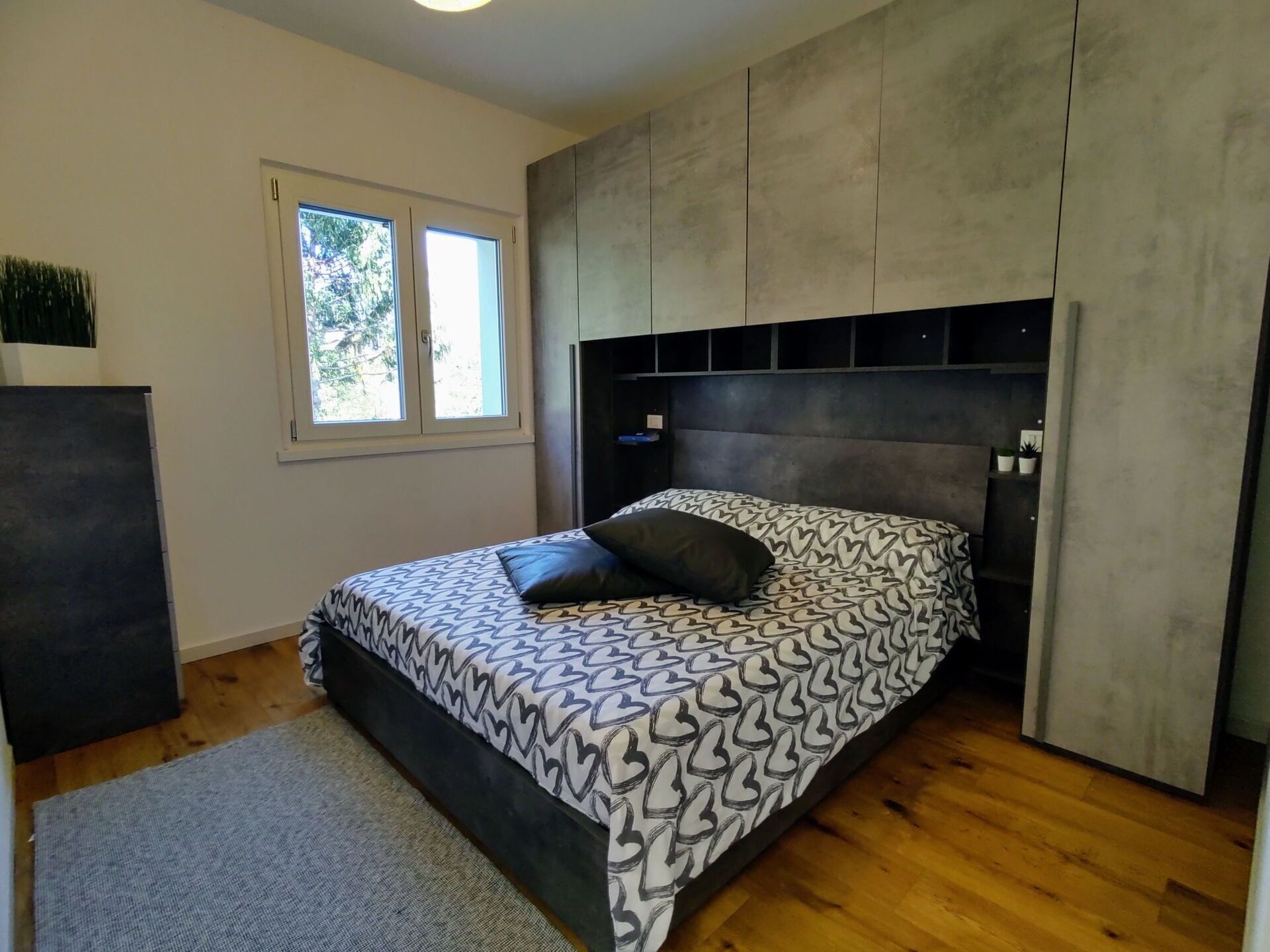 Een slaapkamer met een bed, een raam, een kledingkast en een klein bureau.