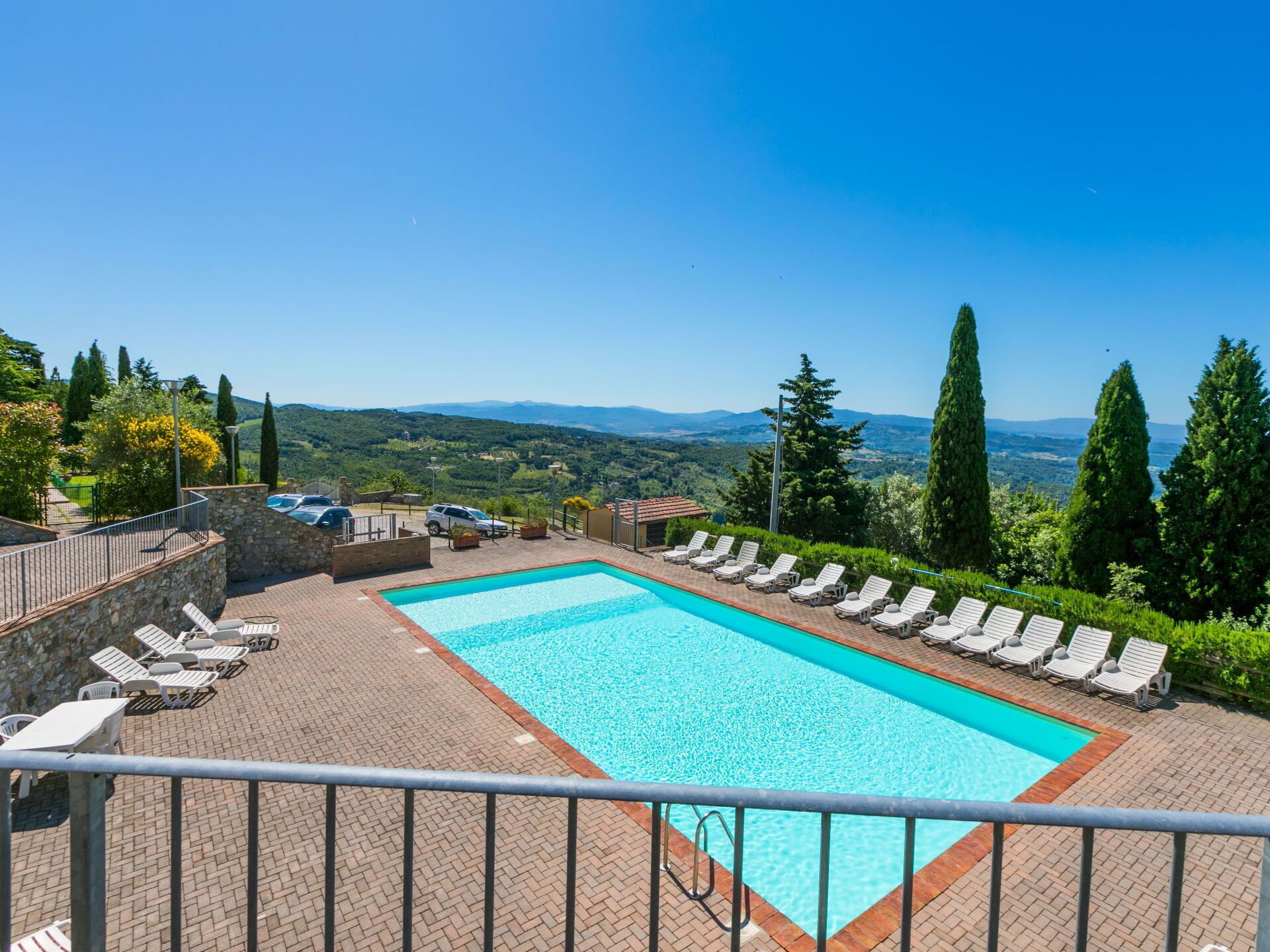A rectangular swimming pool with a clear blue water, surrounded by lounge chairs and a stone wall.