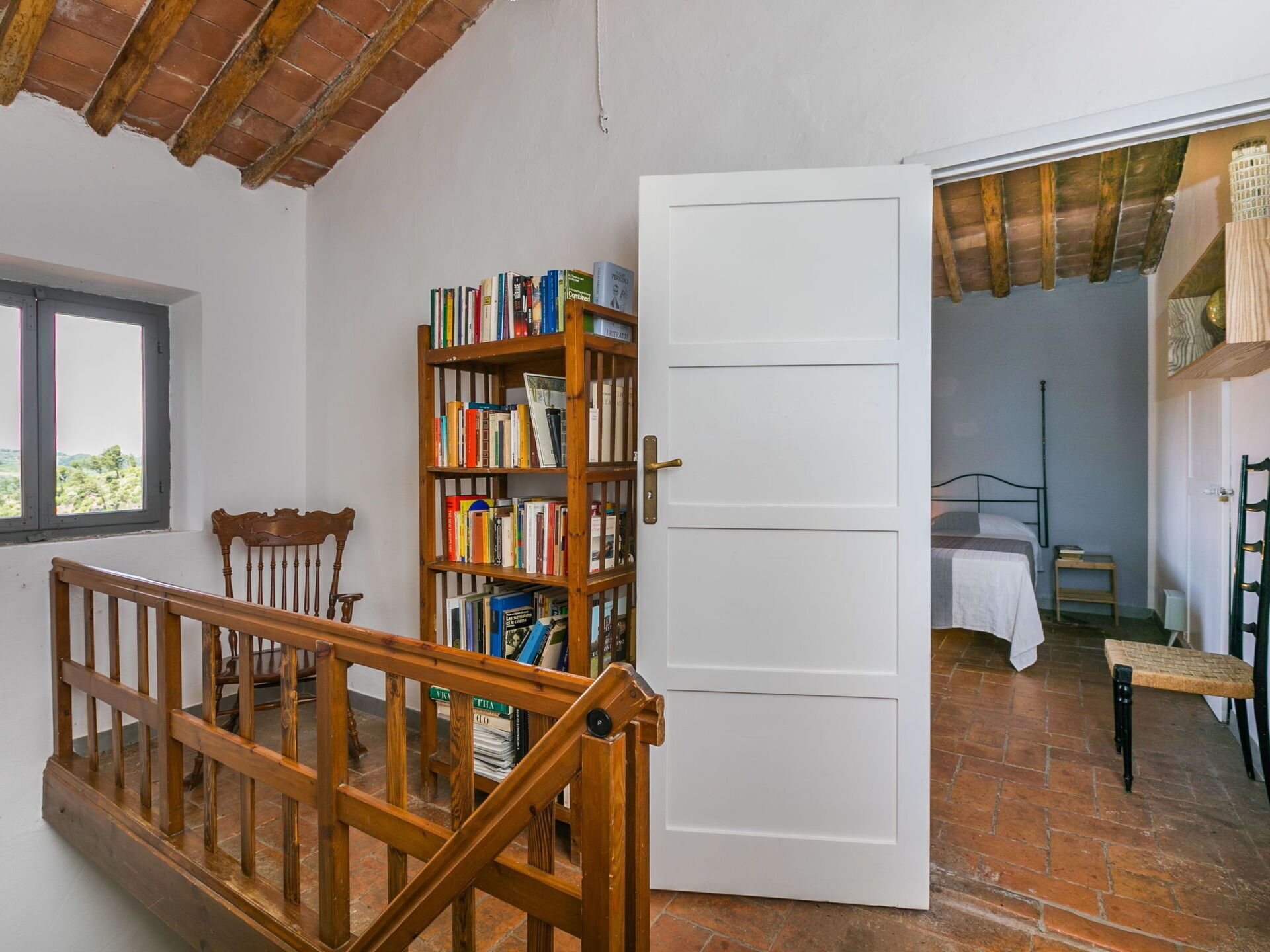 A room with a wooden bookshelf, a bed, a window, and a staircase.