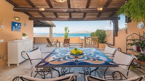Uma área de refeições ao ar livre coberta, com mesa, cadeiras e vista para o mar.