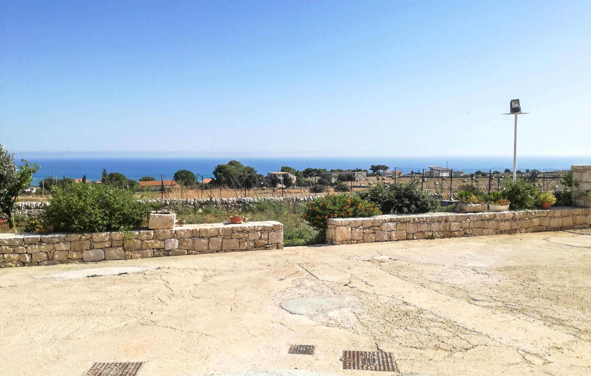 Une vue sur la côte, avec des murs en pierre et des plantes en pot, qui s’ouvre sur une mer bleue et limpide.
