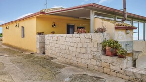 Un bâtiment jaune avec un mur en pierre, des plantes en pot et un petit lavabo.