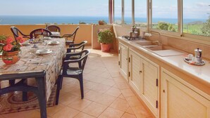 Une terrasse ensoleillée avec une table dressée pour le repas, un évier et une vue sur la mer.