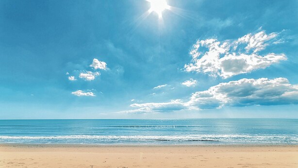 Une plage avec un ciel dégagé, une mer calme et un soleil éclatant.