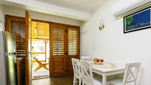 A compact kitchen with a refrigerator, wooden blinds, a dining table with chairs, and a wall-mounted air conditioner.
