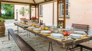 A long dining table set outdoors under a canopy, with plates, glasses, and bottles of wine. - Beautiful private villa for 33 people with private pool, WIFI, TV, patio and pets allowed (San Miniato)