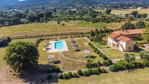 A villa with a swimming pool, surrounded by a well-maintained garden and a view of distant mountains.