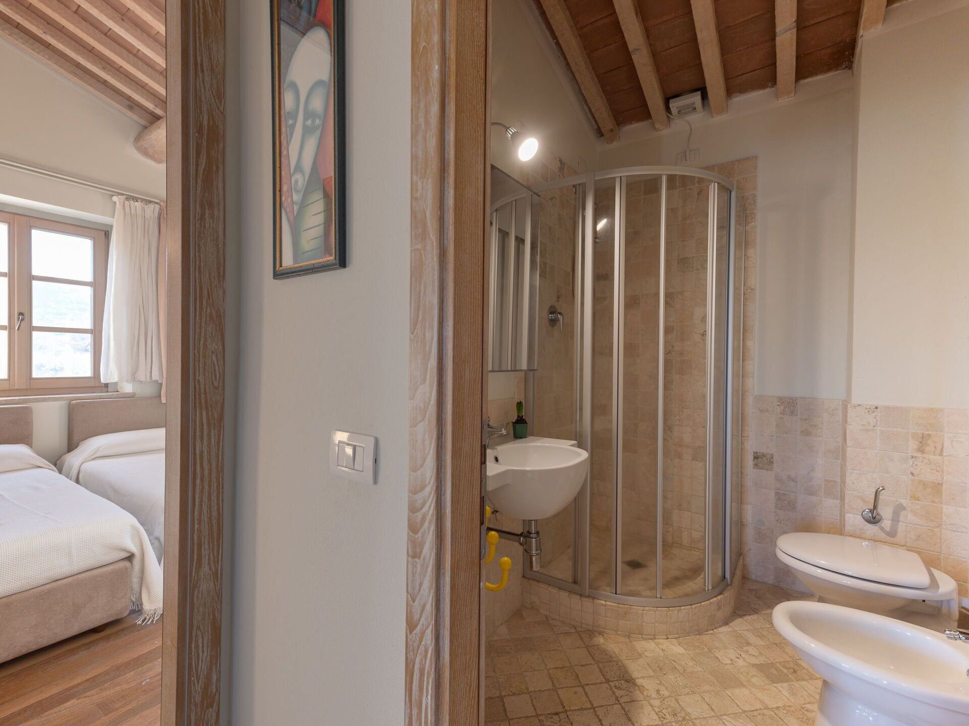Un bany amb dutxa, rentapel i vàter. Es veu un llit a la habitació veïna.