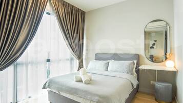 Habitación de hotel moderna con una cama grande, una mesita de noche con lámpara, un espejo y vistas a la ciudad a través de cortinas translúcidas.
