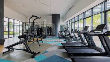 A modern gym with cardio machines, weight training equipment, and large windows offering views of the outdoors.
