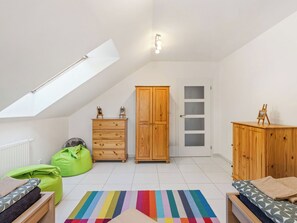 A room with a sloped ceiling, a large wardrobe, a bed with a patterned bedspread, a colorful striped rug, and a green bean bag chair.