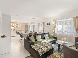 A modern living room with a sofa, a dining table, and a kitchen in the background.