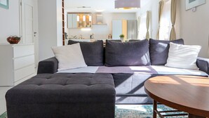 Un salon moderne avec un canapé gris foncé, une table basse ronde en bois et une cuisine en arrière-plan.