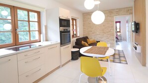 Une cuisine moderne dotée d’un four et d’un micro-ondes encastrés, un coin repas avec des chaises jaunes et un espace de vie comprenant un canapé et un téléviseur.