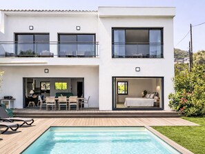 Ein modernes, zweistöckiges Haus mit Swimmingpool, Essbereich im Freien und einem Schlafzimmer mit Blick.