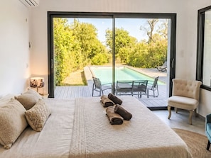 Ein Schlafzimmer mit einem großen Bett, einem Sessel, einem Tisch und Blick auf einen Außenpool.