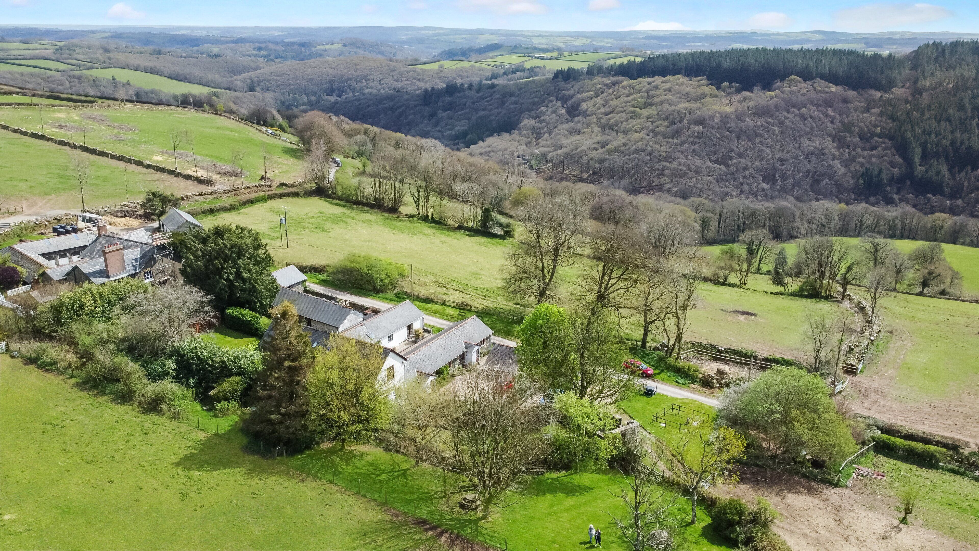 A rural property with a large house, a fenced garden, and a view of the surrounding countryside.