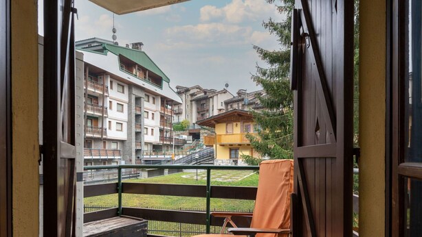 En balkon med en stol og et lille bord, med udsigt over et boligområde med høje bygninger.
