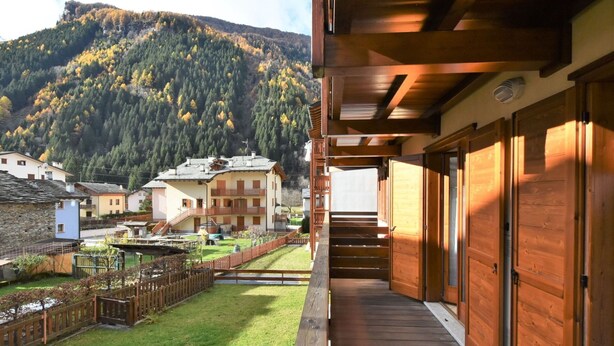 Un balcon en bois offrant une vue sur un paysage montagneux et sur un immeuble doté de nombreux balcons.