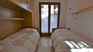 Une chambre avec deux lits, des têtes de lit en bois, une armoire en bois et une vue sur l’extérieur, visible à travers une porte.