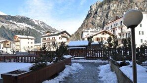 Un sentier enneigé mène à un bâtiment doté de balcons, entouré de montagnes et d’une clôture en bois.