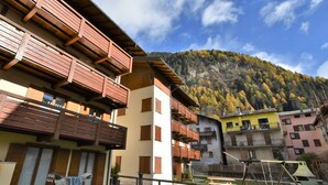 Un immeuble à plusieurs étages doté de balcons en bois, une cour avec une table de pique-nique et un paysage montagneux en arrière-plan.