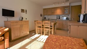 Une chambre d’hôtel compacte comprenant un lit, une petite kitchenette, un coin repas avec une table et des chaises, et un téléviseur fixé au mur.