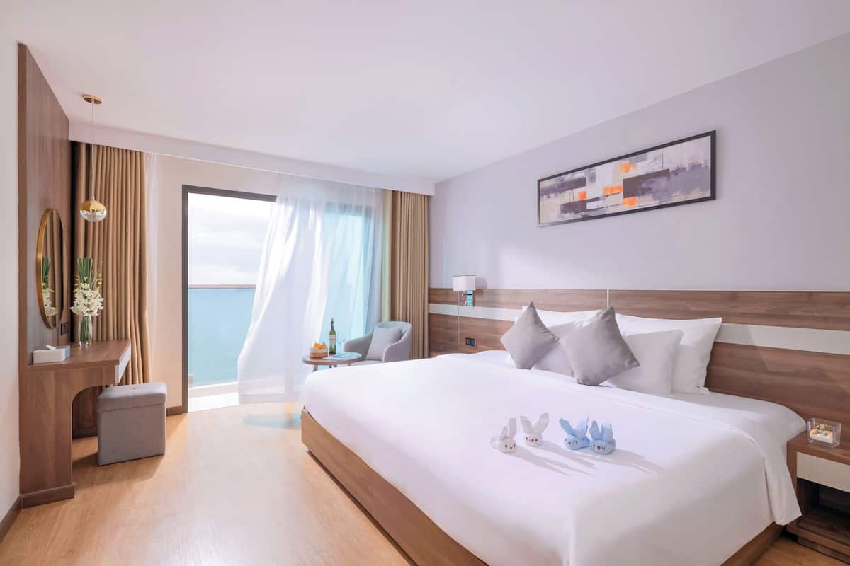 Hotelkamer met een groot bed, een bureau, een stoel, een klein tafeltje met een fles en uitzicht op zee.