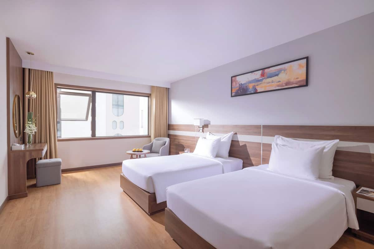 Een hotelkamer met twee bedden, een bureau, een stoel, een klein tafeltje en een raam met gordijnen.