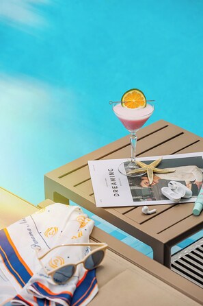 Un salon de plage avec un cocktail, un magazine et une étoile de mer posés sur une table en bois.