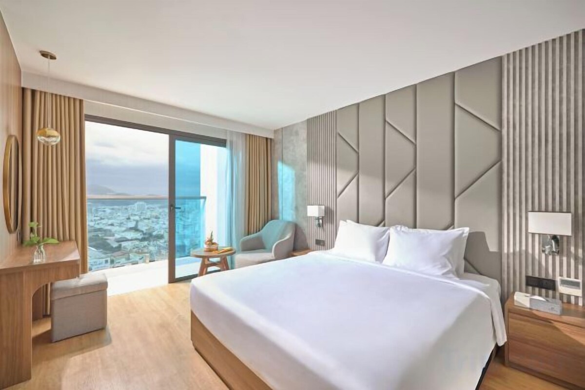 Una habitación de hotel moderna con una cama grande, un escritorio, una silla y vistas a la ciudad.
