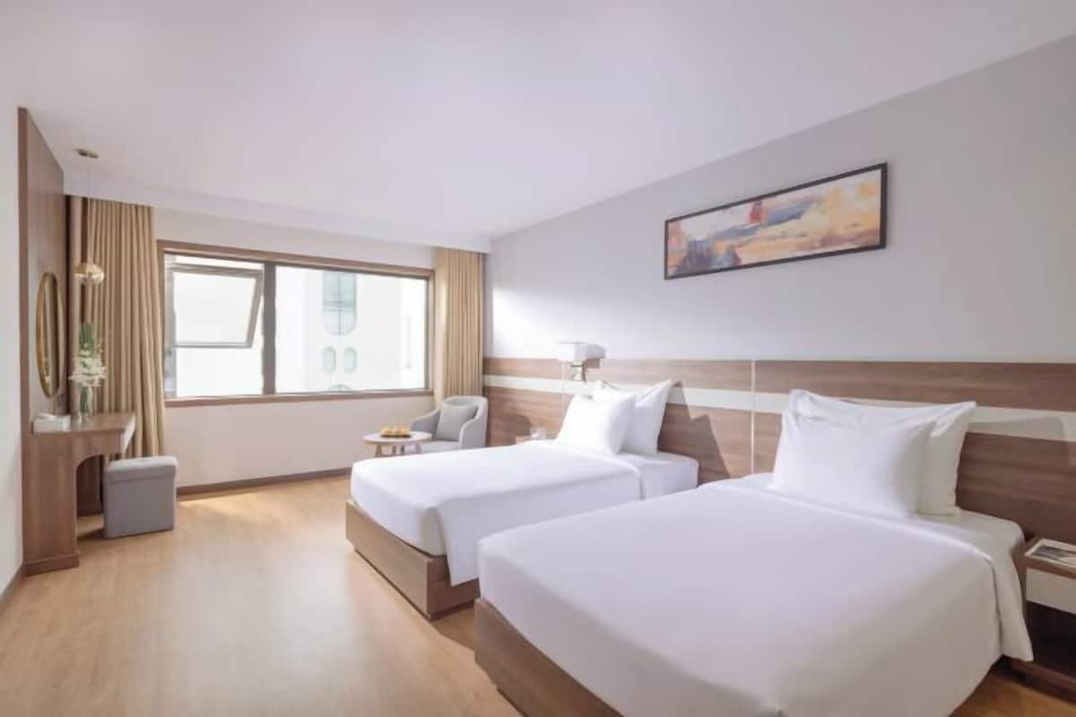 Een hotelkamer met twee bedden, een bureau, een stoel, een raam en een schilderij aan de muur.