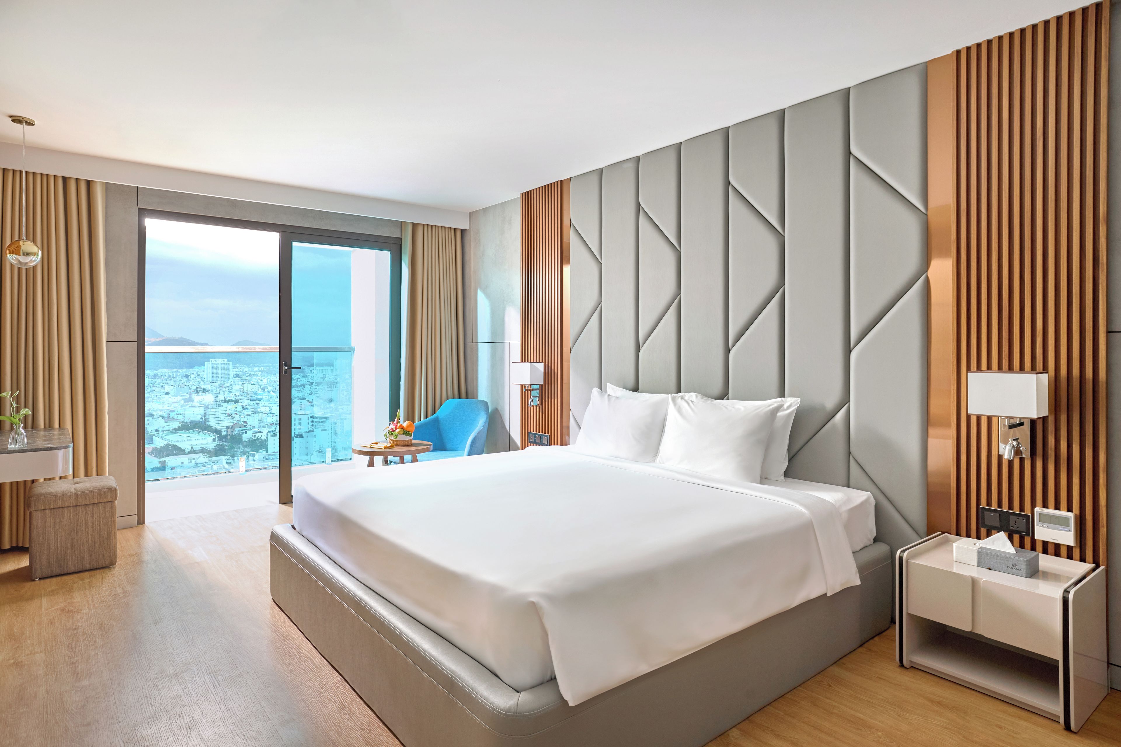 Ein modernes Hotelzimmer mit einem großen Bett, Stadtblick, einem blauen Sessel und einem kleinen Tisch mit einer Vase.
