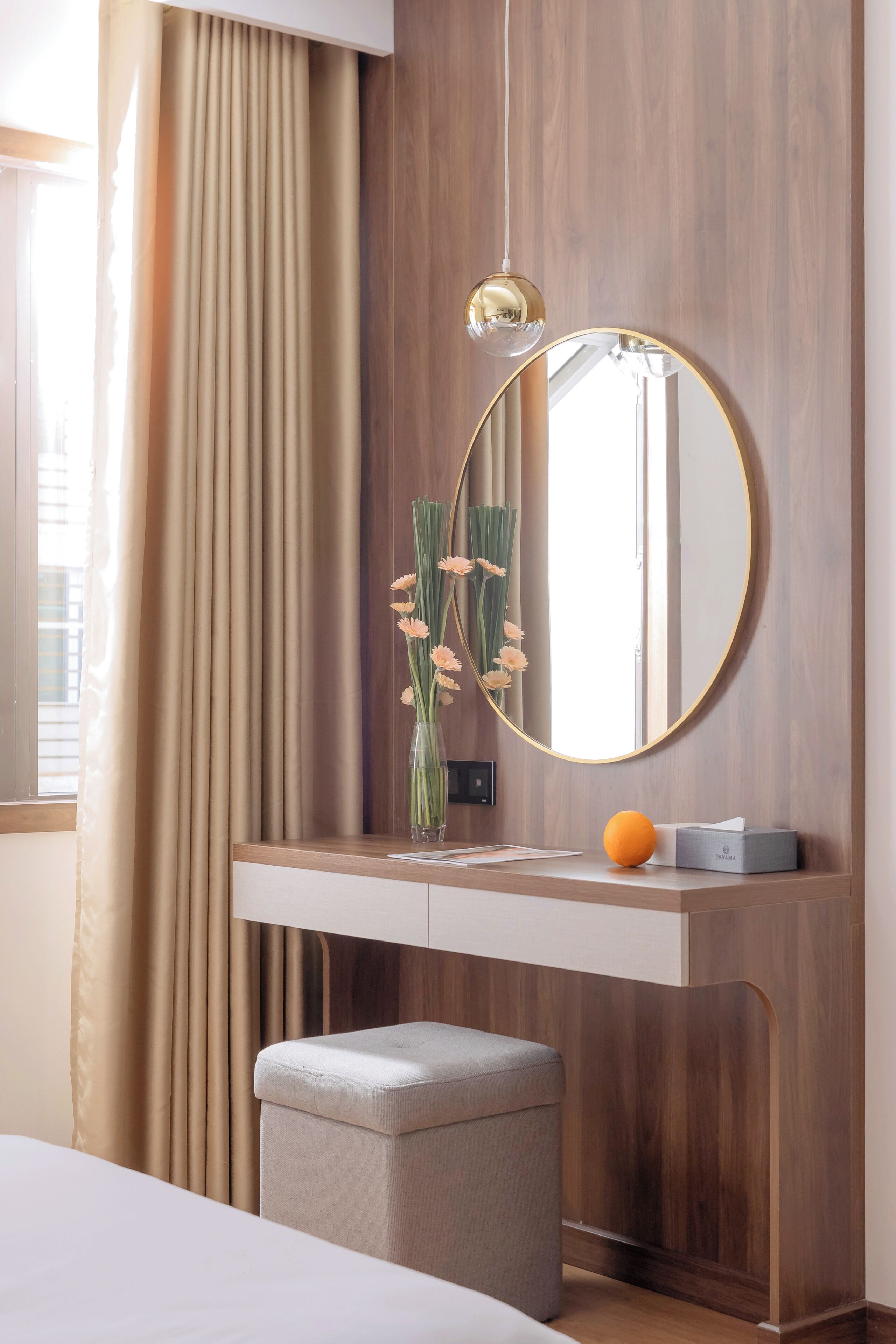 Een moderne kamer met een houten wand, een ronde spiegel, een bureau met een bloevas en een klein sinaasappel op het bureau.