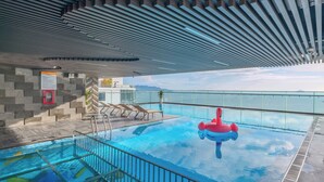 An indoor swimming pool with clear blue water, a red flamingo float, and a glass balustrade overlooking a body of water. - PANAMA Nha Trang Hotel (Nha Trang)