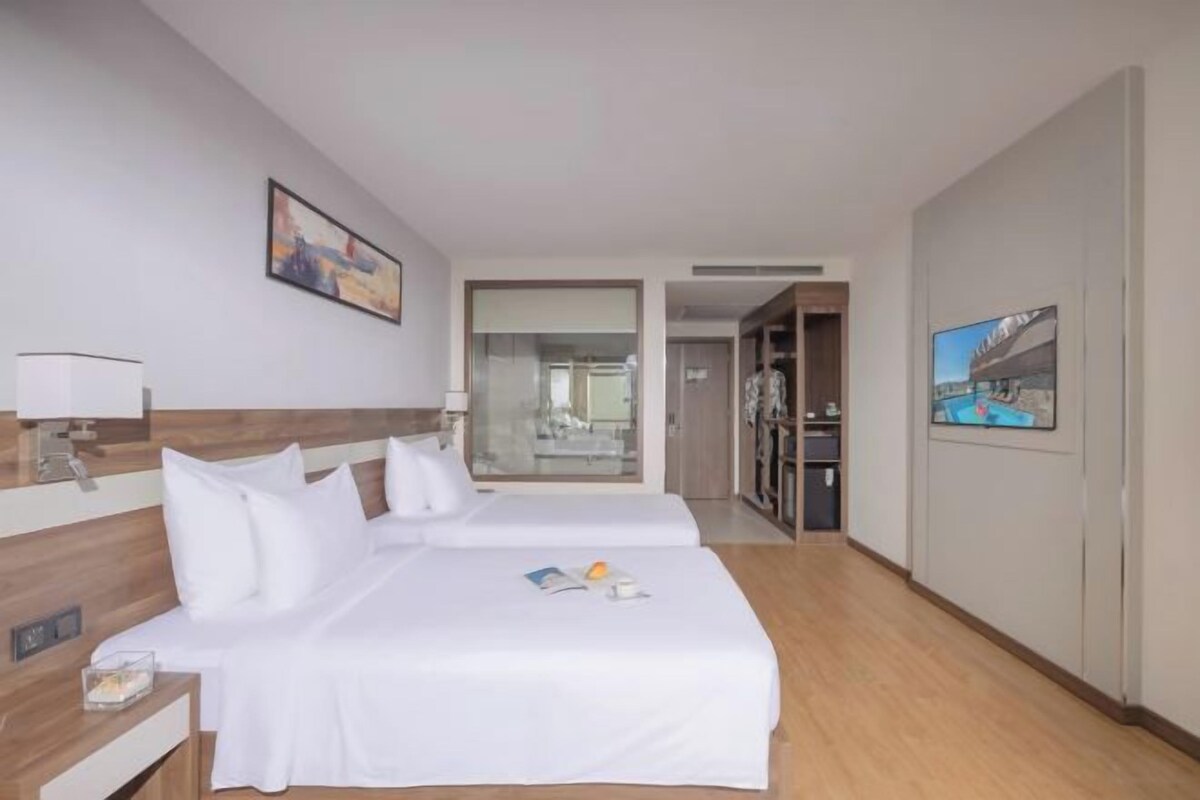 A hotel room with two beds, a desk, a mirror, and a door leading to a bathroom.