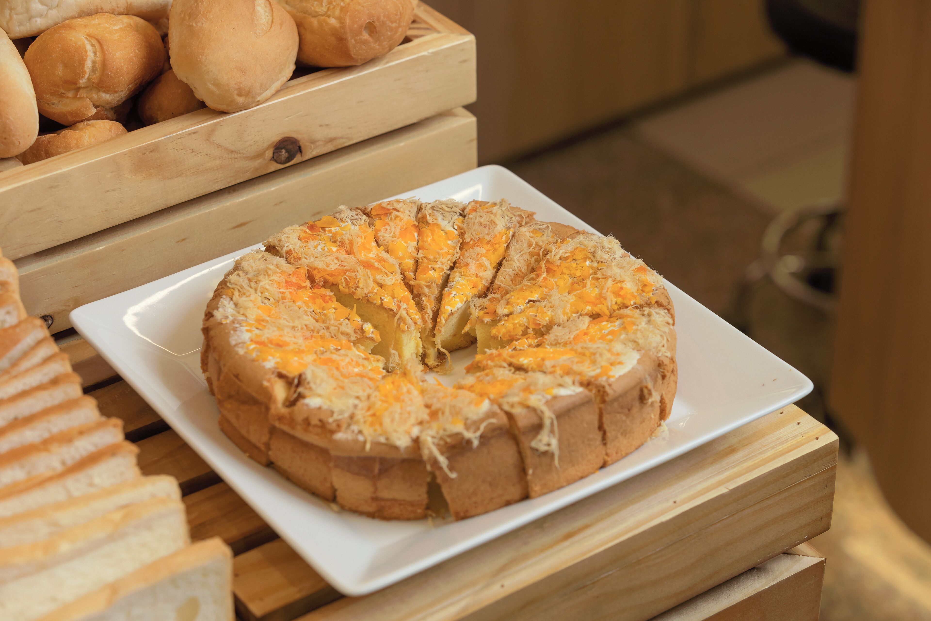 A round cake with shredded cheese on a white plate, placed on a wooden table.