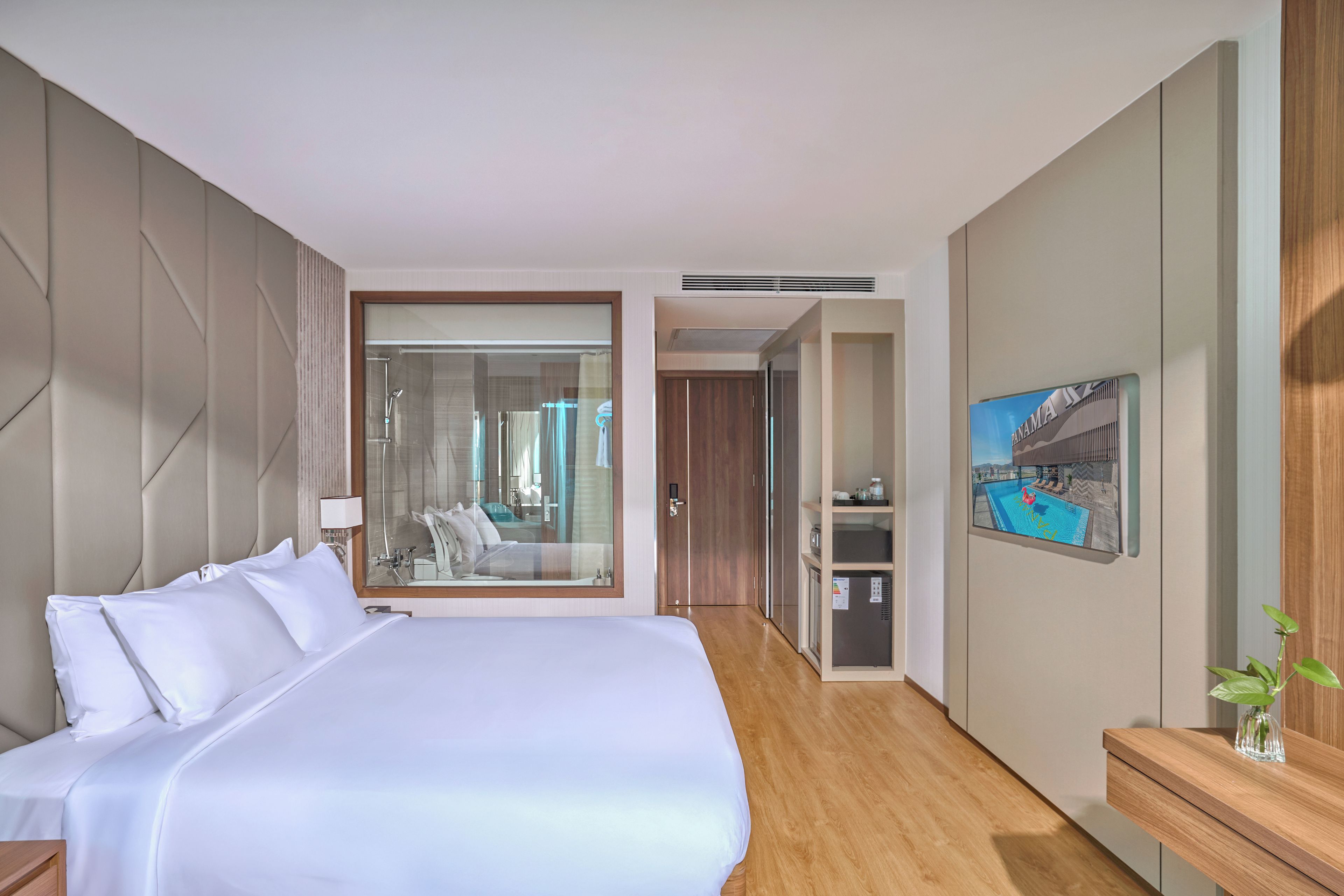Une chambre d’hôtel moderne dotée d’un grand lit, d’une salle de bain avec une douche en verre, d’un petit coin cuisine et donnant sur une piscine.