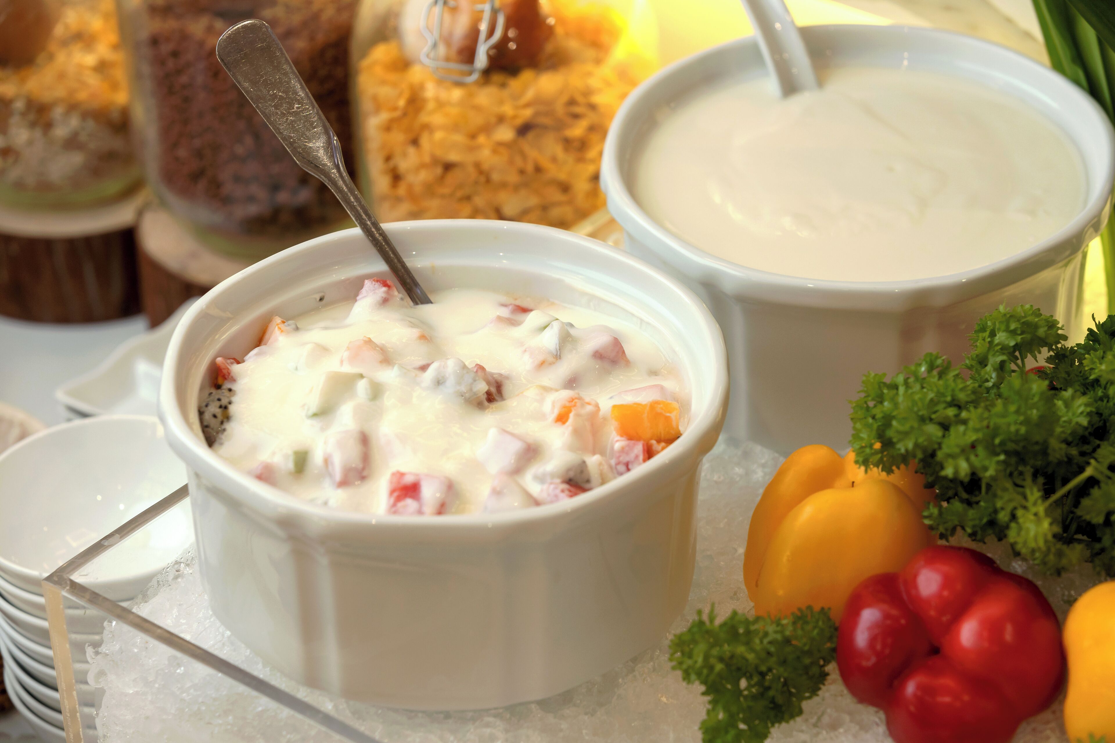 A bowl of creamy soup with a spoon, surrounded by vegetables and bread.