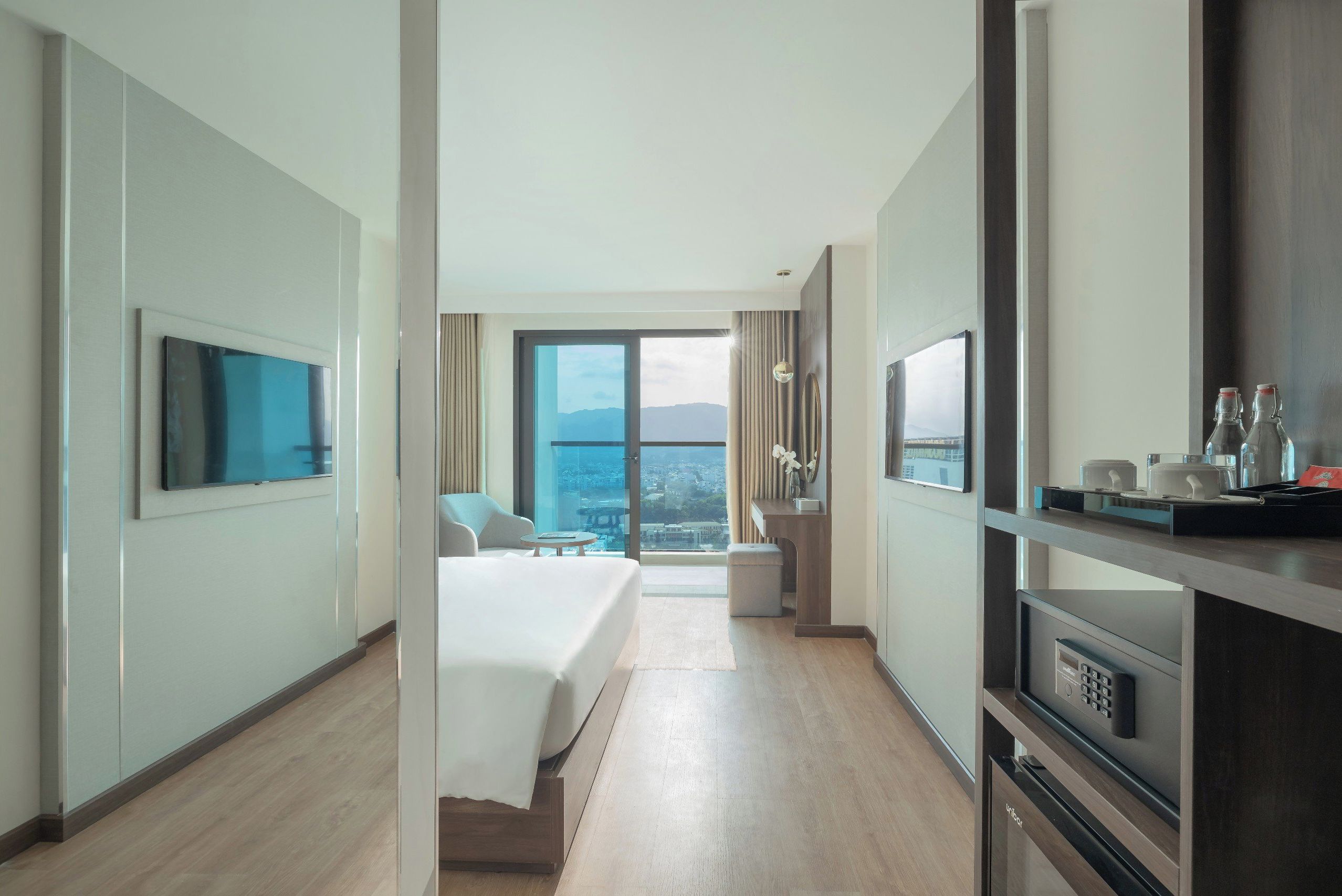 Una camera d'albergo moderna con un letto grande, una TV a muro, angolo cottura e un balcone con vista sulla città.
