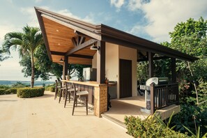Relax by the outdoor bar, surrounded by lush greenery and a pergola, with a grill and bar stools at your disposal.