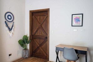 Ein Zimmer mit Holztür, Schreibtisch mit Stuhl, einer Topfpflanze, Wanddekoration und einem gerahmten Bild.