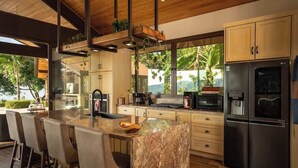 A modern kitchen with a marble island, stainless steel appliances, and a view of greenery outside.